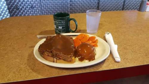 A plate with two slices of bread topped with brown gravy, a scoop of mashed potatoes, and a side of carrot slices.