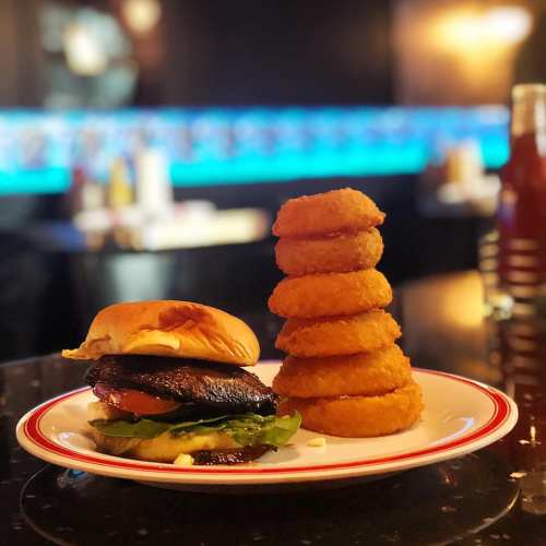 A juicy burger with lettuce and sauce, accompanied by a tall stack of golden onion rings on a plate.