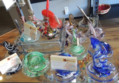 Colorful glass art pieces displayed on a table, featuring swirls and unique designs, with price tags visible.