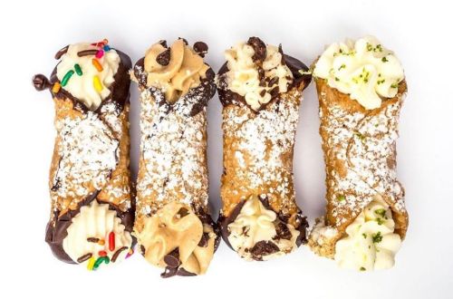 Four delicious cannoli filled with cream, topped with sprinkles and chocolate, dusted with powdered sugar.