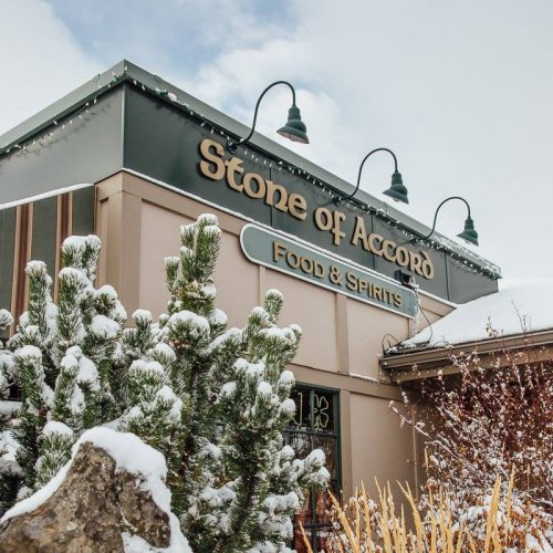 Sign for "Stone of Accord Food & Spirits" on a snowy day, with evergreen trees in the foreground.