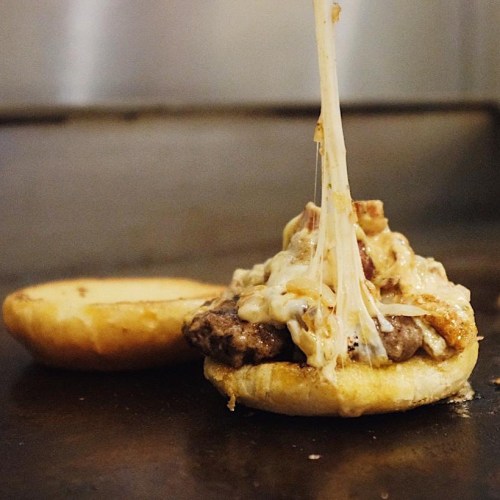 Melted cheese drips from a juicy burger patty on a toasted bun, ready to be topped and served.