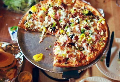 A freshly baked pizza topped with cheese, meats, olives, and peppers, served on a metal pizza tray.