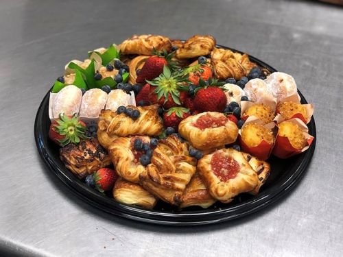 A platter of assorted pastries, including fruit tarts, doughnuts, and muffins, garnished with strawberries and blueberries.