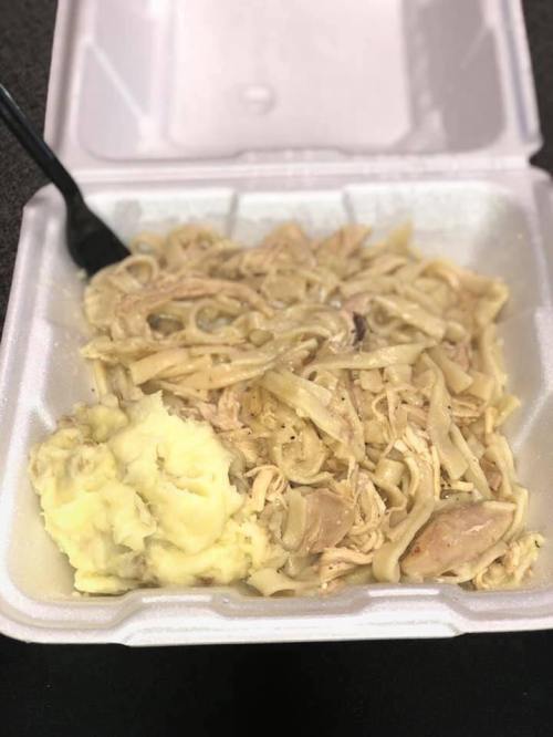 A takeout container with creamy chicken and noodles alongside a serving of mashed potatoes.