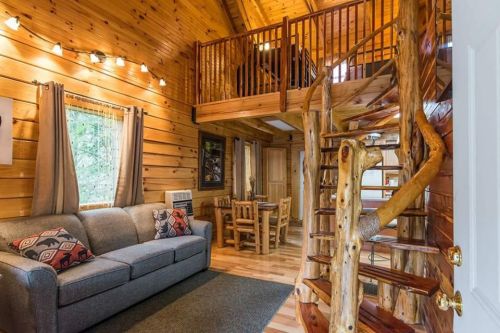 Cozy wooden cabin interior with a spiral staircase, sofa, dining area, and warm lighting.