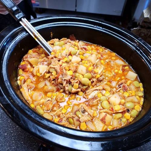 A close-up of a slow cooker filled with a hearty stew featuring chicken, potatoes, corn, and green beans.