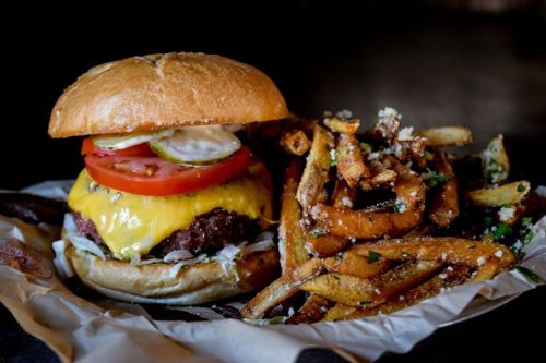 A juicy cheeseburger with lettuce, tomato, and pickles, served with a side of crispy fries on parchment paper.