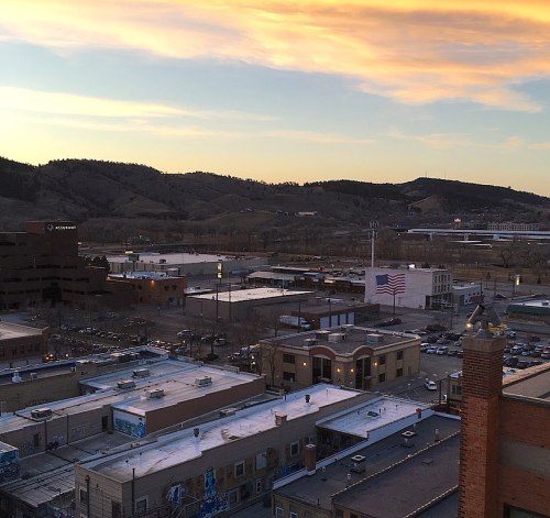 A panoramic view of a cityscape at sunset, with mountains in the background and an American flag visible.