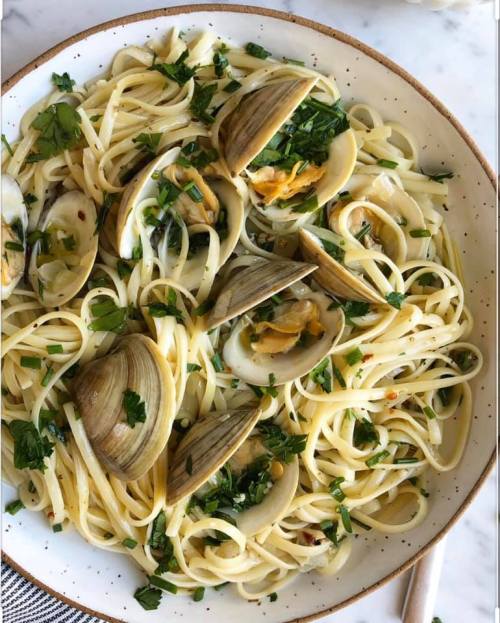 A plate of linguine pasta topped with clams and fresh parsley, garnished with red pepper flakes.