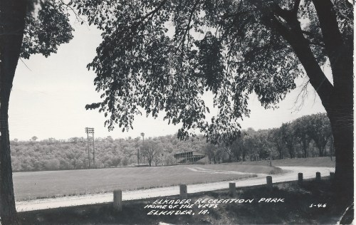 Black and white photo of Elkader Recreation Park, framed by trees, featuring a field and distant bleachers.