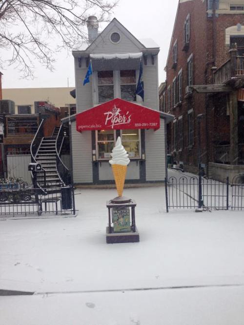 A snow-covered street scene featuring an ice cream stand with a large ice cream cone sign in front of a building.