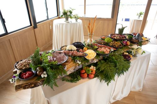 A beautifully arranged buffet table featuring various dishes, meats, cheeses, and fresh vegetables, surrounded by greenery.