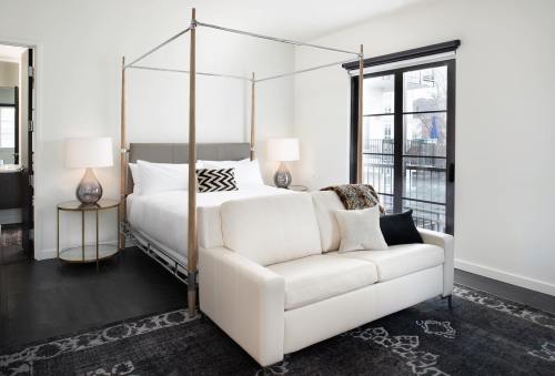 Modern bedroom featuring a four-poster bed, white sofa, and large windows with natural light.
