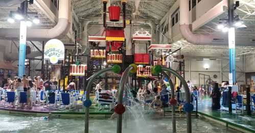 A vibrant indoor water park with a large play structure, water features, and families enjoying the space.