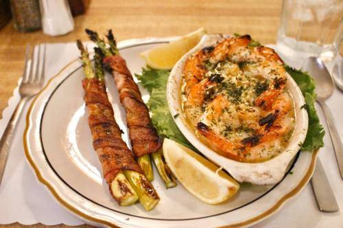 A plate featuring baked shrimp with herbs, lemon wedges, and bacon-wrapped asparagus on the side.