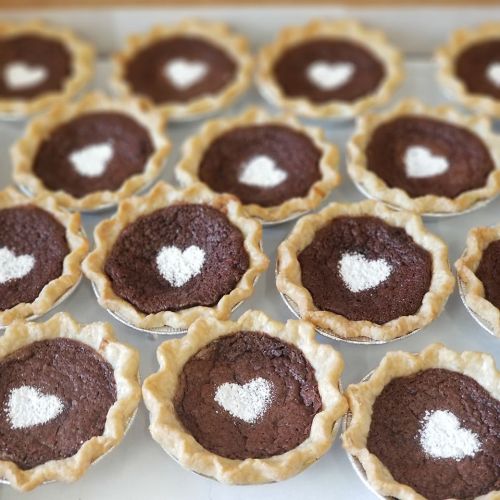 A tray of mini chocolate pies, each with a heart-shaped dusting of powdered sugar on top.