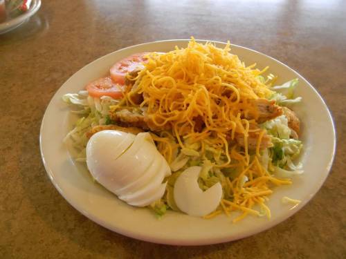 A plate of salad topped with shredded cheese, sliced tomatoes, and a boiled egg on a bed of lettuce.