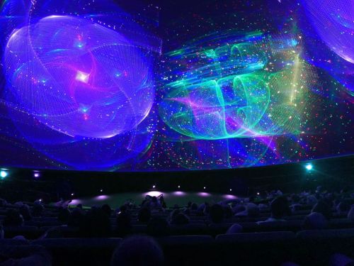 A vibrant, colorful light display projected on a dome, with an audience seated below, enjoying the visual experience.
