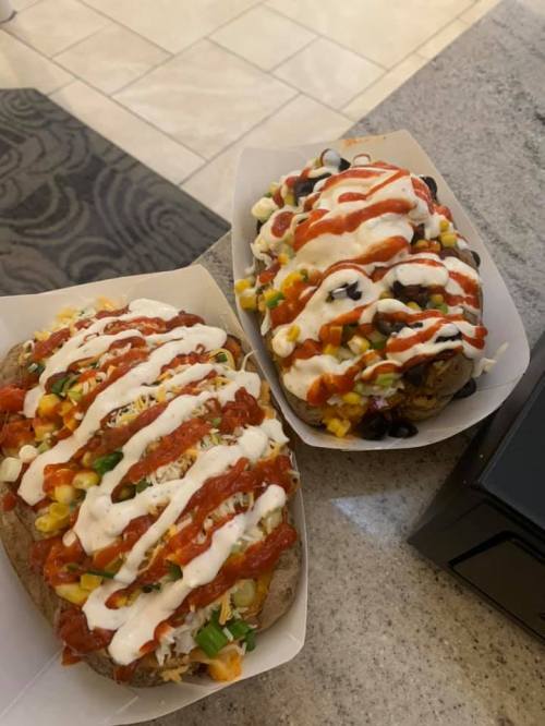 Two loaded baked potatoes topped with salsa, sour cream, corn, black beans, and diced tomatoes on a countertop.