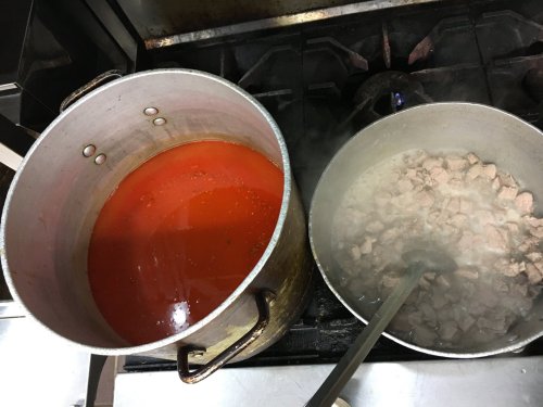 Two large pots on a stove: one with simmering red sauce and the other with cooked, diced meat. Steam rising from both.