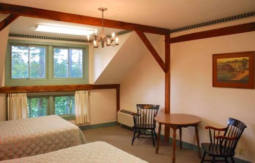 Cozy room with two beds, a table, and chairs, featuring wooden beams and large windows overlooking greenery.