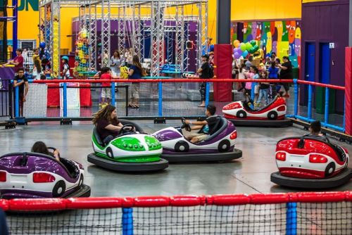 Children enjoy bumper cars in a colorful indoor amusement area, surrounded by playful decorations and other attractions.