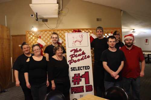 A group of eight people poses in a restaurant, celebrating a "#1 Prime Rib" award with festive decorations.