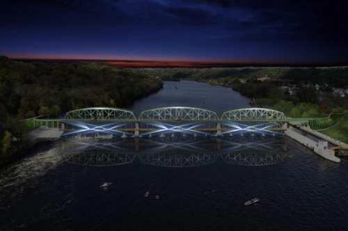 A modern bridge illuminated at night spans a river, reflecting in the water, surrounded by trees and a twilight sky.