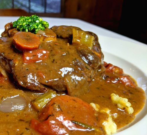 A close-up of a savory beef dish with carrots, celery, and broccoli, served on a white plate.