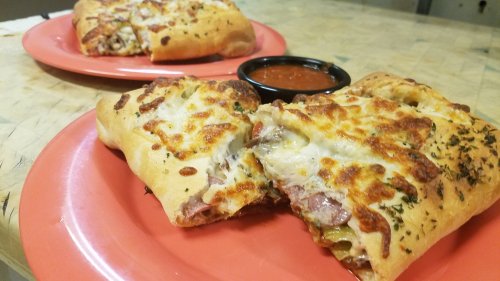 Two stuffed calzones on orange plates, one cut open to reveal filling, served with a side of marinara sauce.
