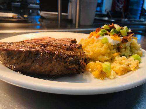 A plate featuring a grilled steak alongside creamy mashed potatoes topped with green onions and bacon bits.