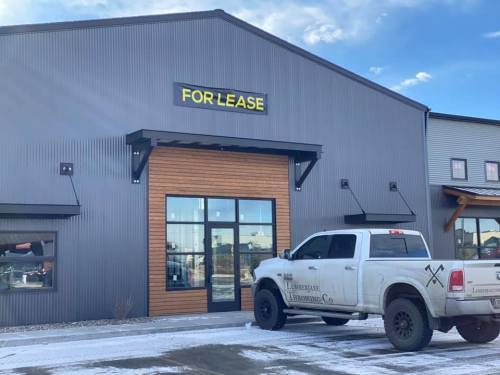 A commercial building with a "For Lease" sign and a truck parked outside on a snowy day.