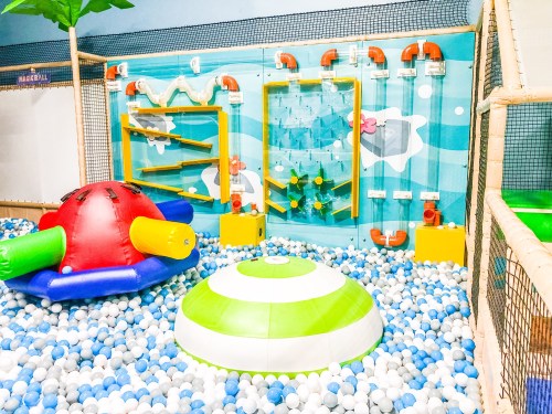 Colorful indoor play area with a ball pit, climbing wall, and interactive water features for children.