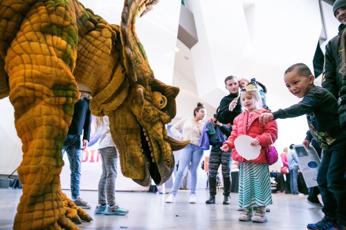 A colorful dinosaur costume interacts with excited children at an event, creating a fun and lively atmosphere.