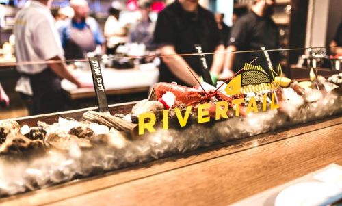 A seafood display featuring a lobster and oysters, with the word "RIVERTAIL" prominently featured in the foreground.