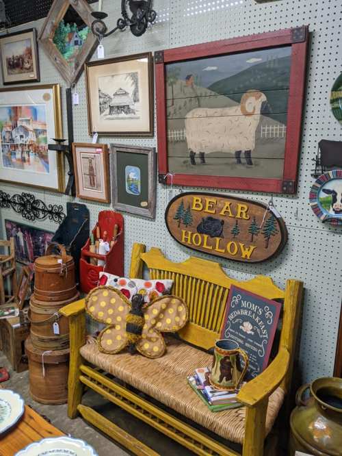 A cozy display of vintage decor, including a yellow bench, framed art, and whimsical butterfly and bear signs.