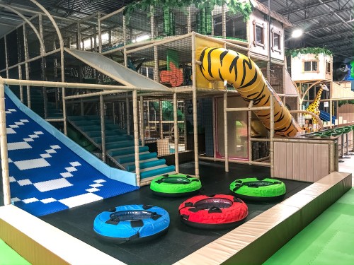 Colorful indoor play area featuring slides, climbing structures, and inflatable tubes.