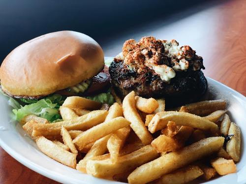 A juicy burger topped with popcorn and spices, served with a side of golden French fries on a white plate.