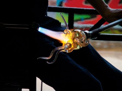 A close-up of a glassblower shaping molten glass with a flame, creating intricate designs.