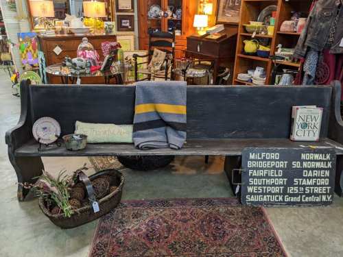 A vintage bench with a blanket, decorative items, and a book in a cozy antique shop setting.
