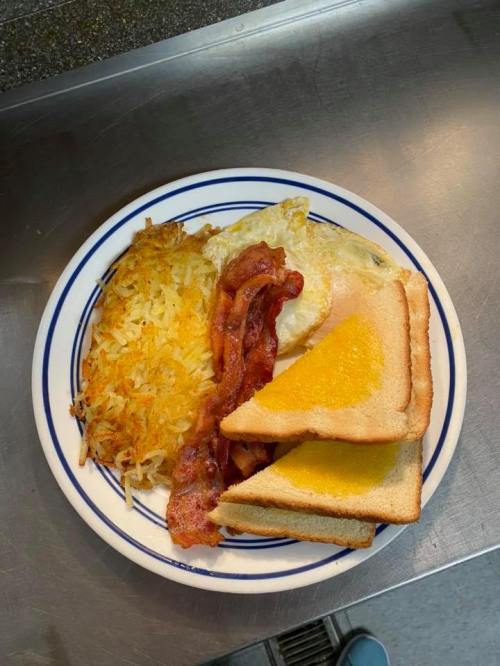 A plate with scrambled eggs, crispy bacon, hash browns, and buttered toast.