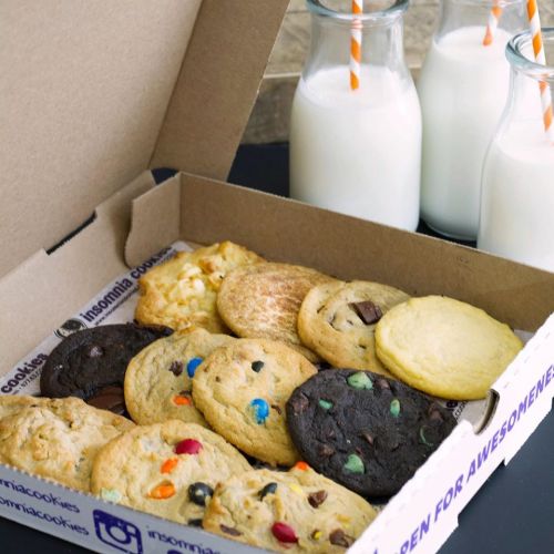 A box of assorted cookies with two bottles of milk in the background, featuring colorful sprinkles and chocolate chips.