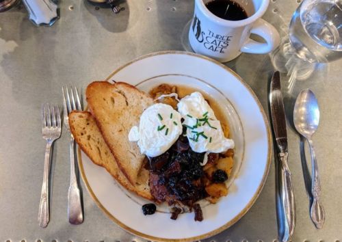 A plate of poached eggs on a savory dish with toast, alongside a cup of coffee and a glass of water.
