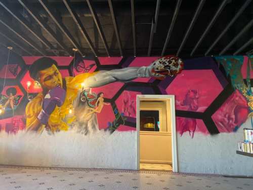 A vibrant mural of a boxer throwing a punch, surrounded by colorful butterflies and geometric patterns.