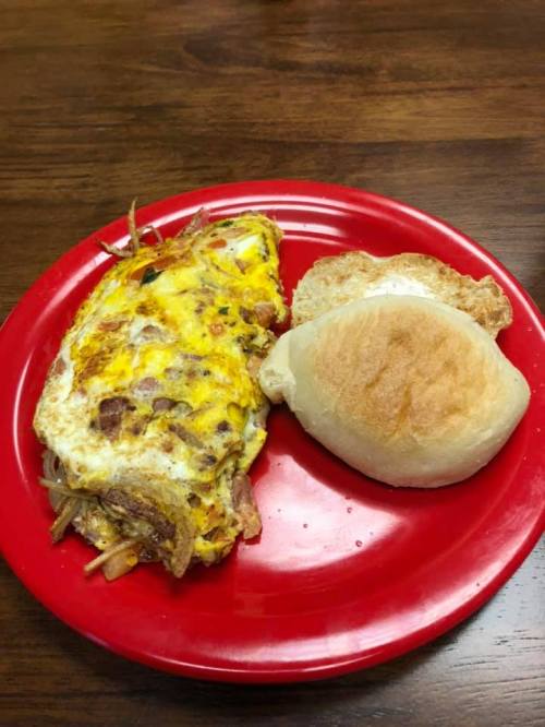 A red plate with a vegetable omelet and a soft bread roll on a wooden table.