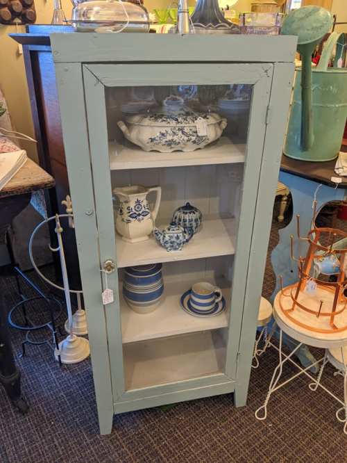 A vintage glass-front cabinet displaying blue and white dishware on shelves, set in a cozy shop environment.