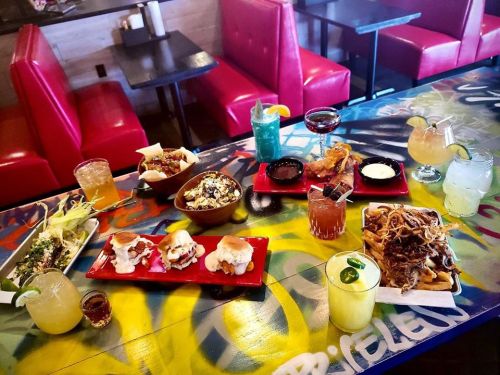 A vibrant table spread with various colorful dishes and drinks, set against a graffiti-style background.