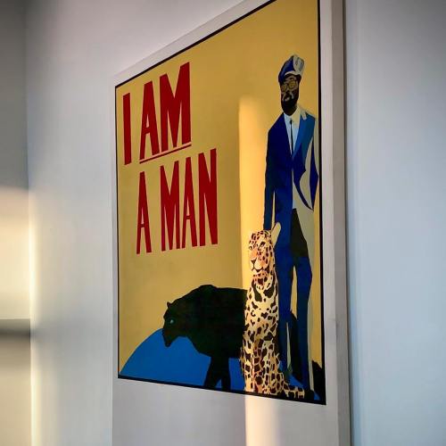 A colorful poster featuring a man in a suit with a leopard and a panther, alongside the text "I AM A MAN."