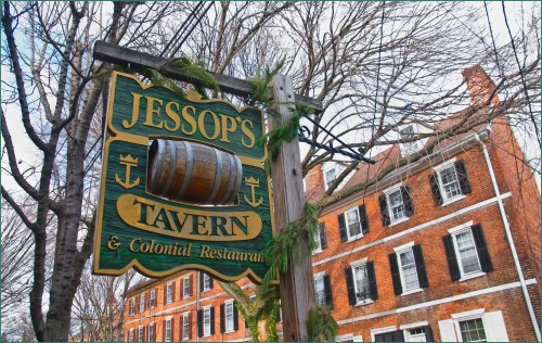 Sign for Jessop's Tavern & Colonial Restaurant, featuring a barrel and surrounded by trees and historic brick buildings.